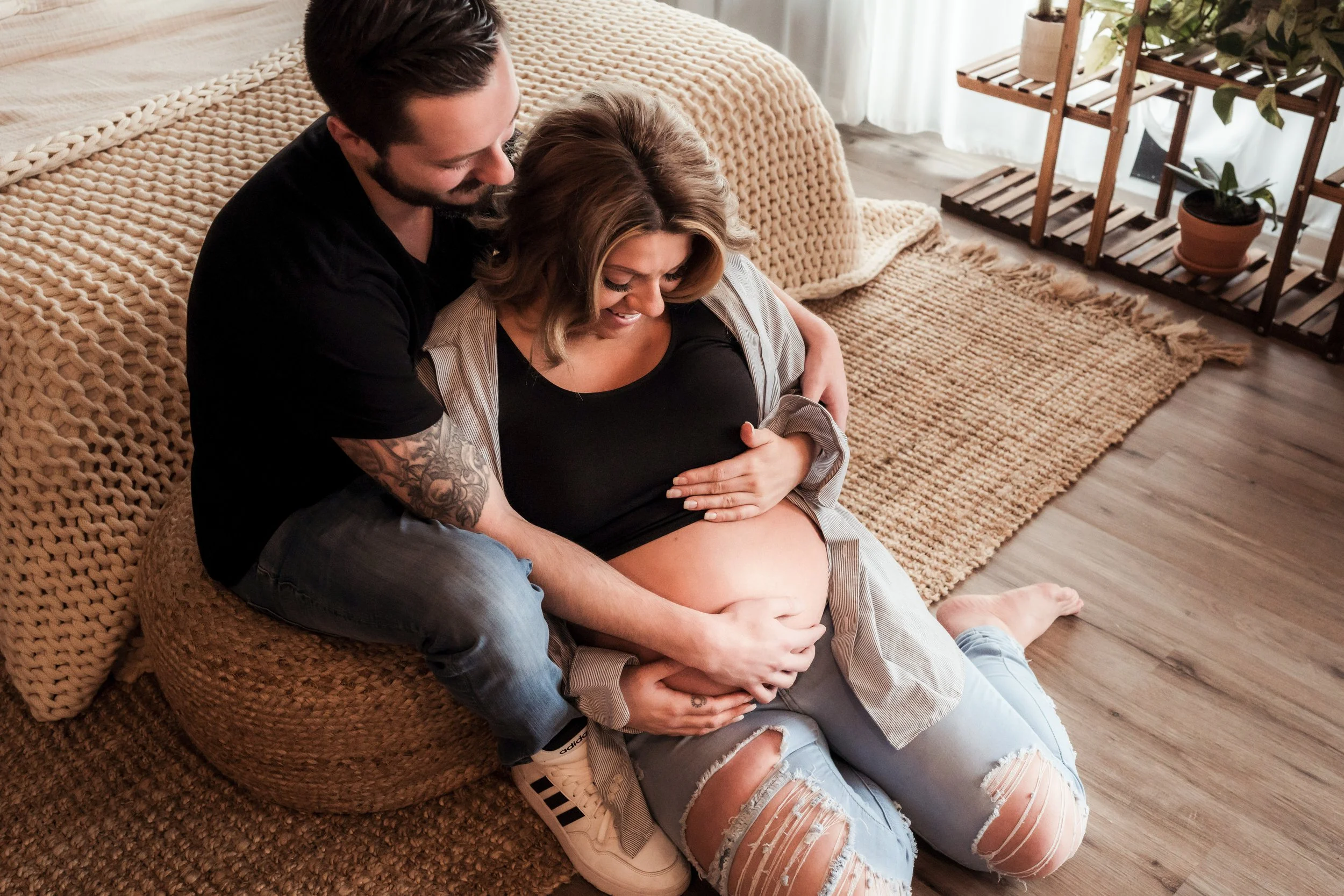 Expectant parents sitting together on the floor in a cozy, softly lit room, gently holding and admiring the mother’s baby bump.