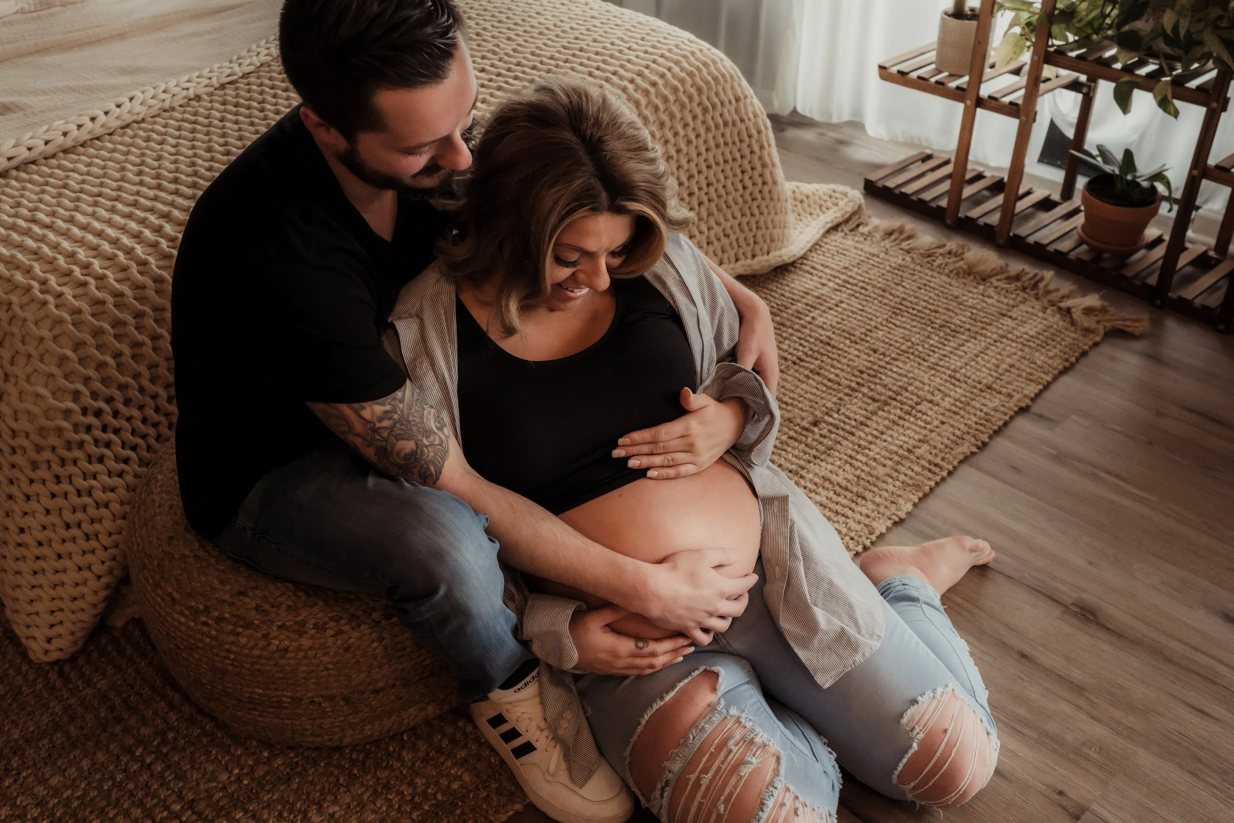 Expectant parents sitting together on the floor in a cozy, softly lit room, gently holding and admiring the mother’s baby bump.
