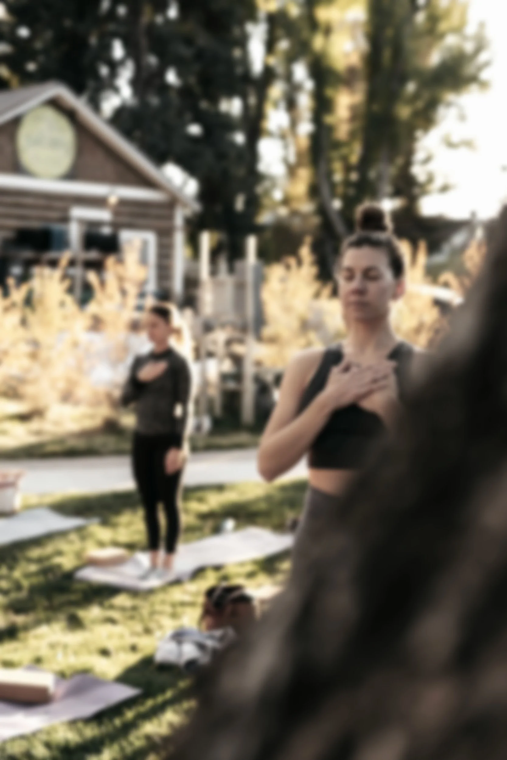 Two women practicing yoga outdoors in a backyard with trees and a building in the background during sunset.