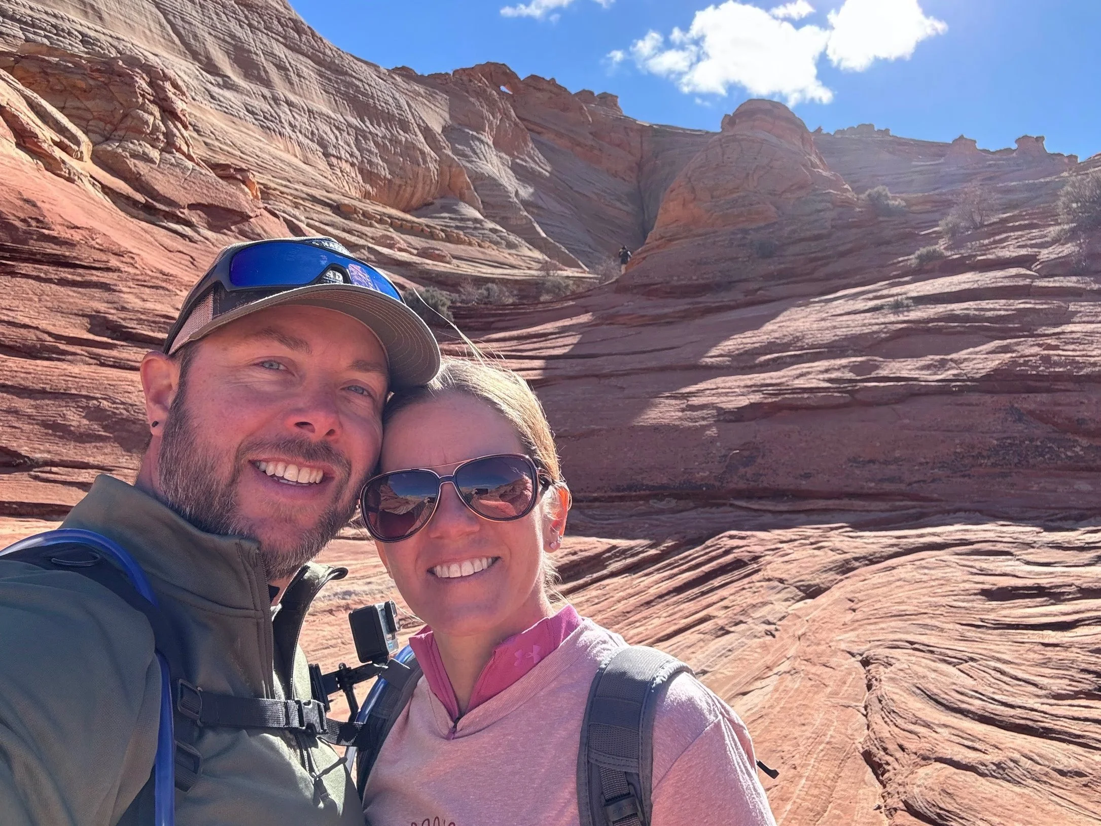 Kaven et Sophie souriant en randonnée dans un paysage désertique avec des formations rocheuses rouges et un ciel bleu.