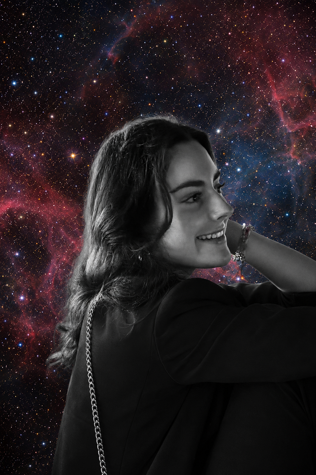 A young woman with dark, wavy hair smiling and looking to her left, dressed in dark clothing with a chain strap, set against a colorful starry galaxy background.