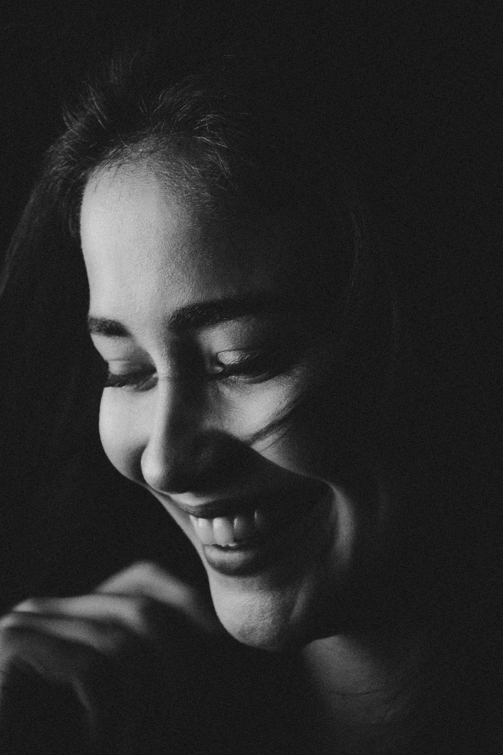 black and white portrait of woman looking down and smiling, showing teeth