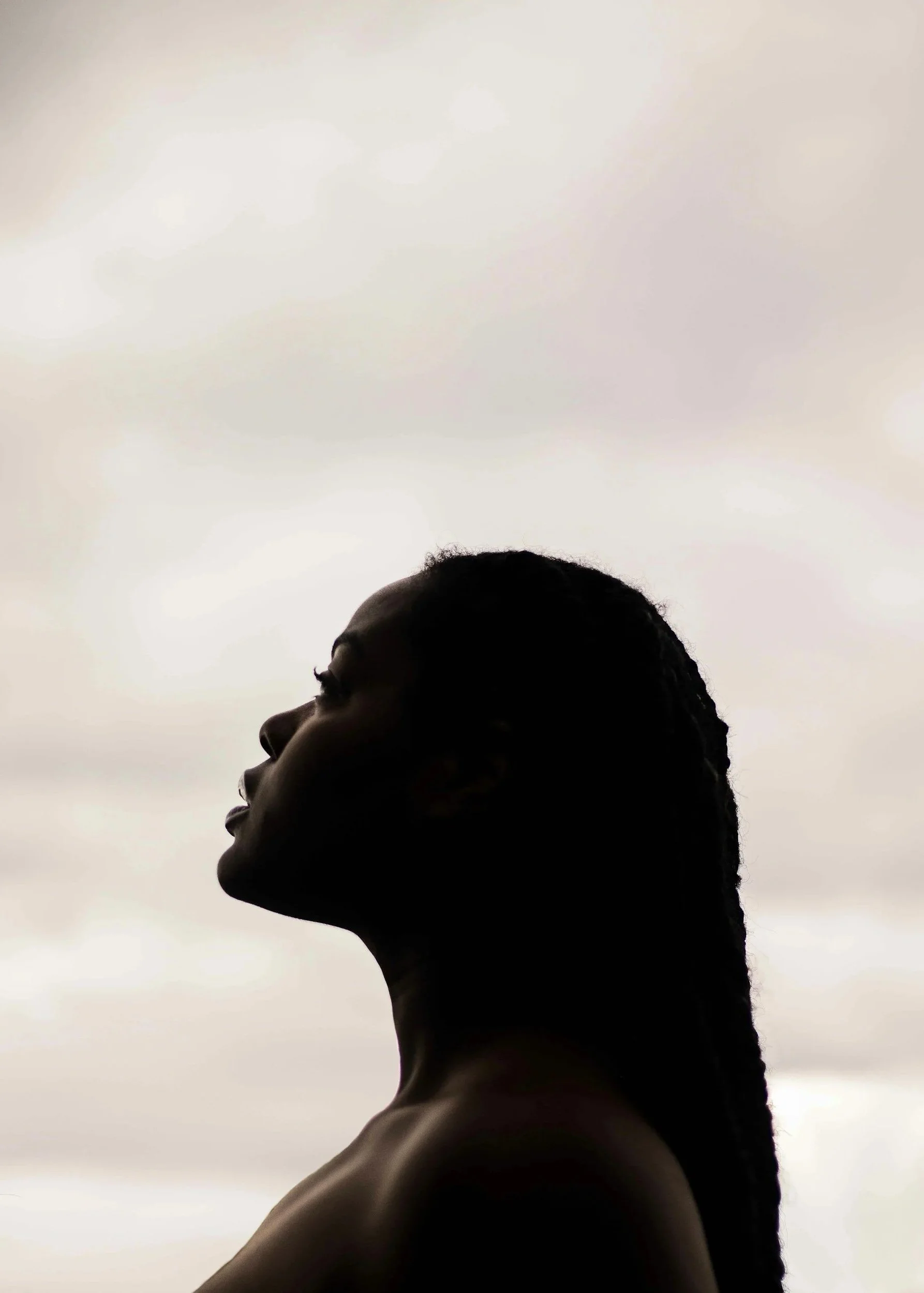 Silhouette of a woman with braided hair looking upwards against a cloudy sky.