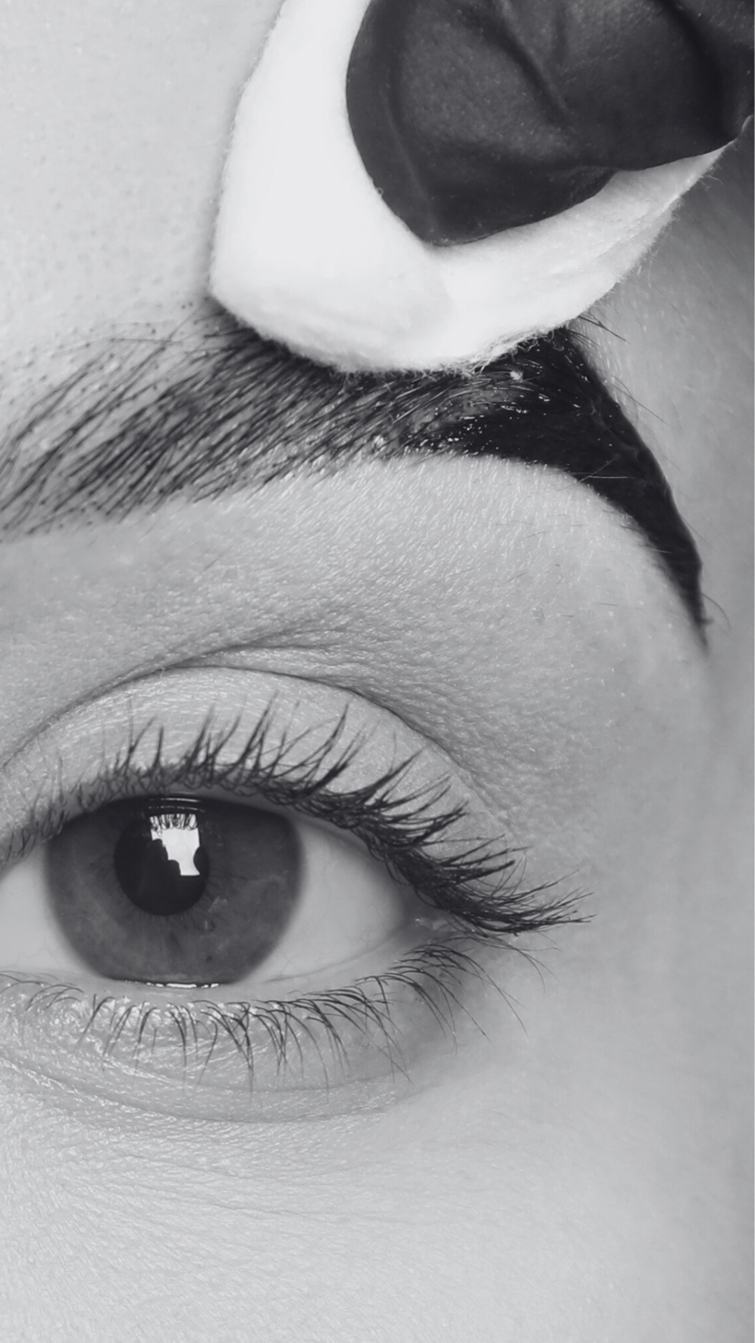 Close-up of a person's eye, eyelashes, eyebrow, nose, and lips in black and white.