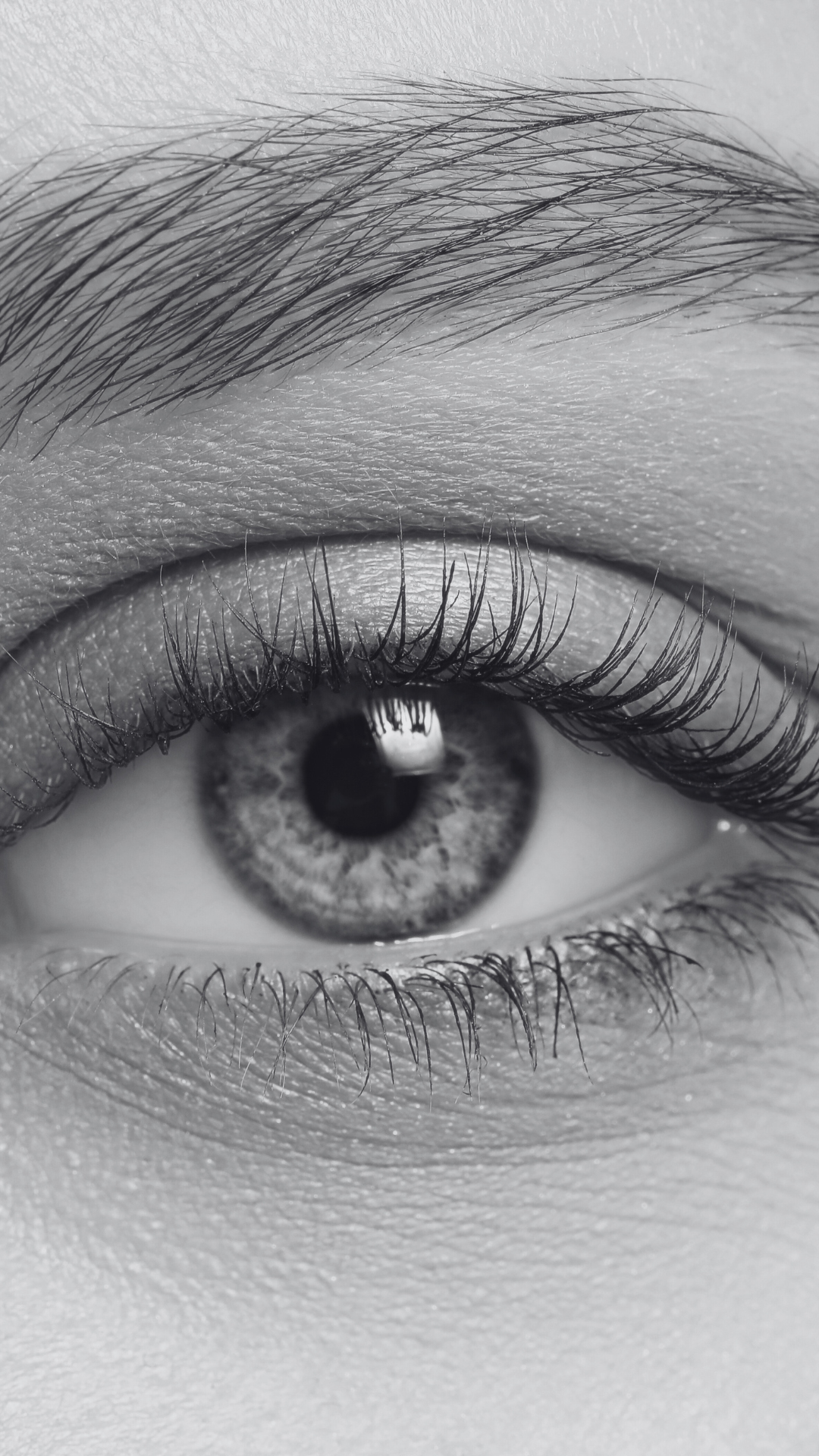 Close-up black and white photo of a human eye with detailed iris, eyelashes, and surrounding skin.