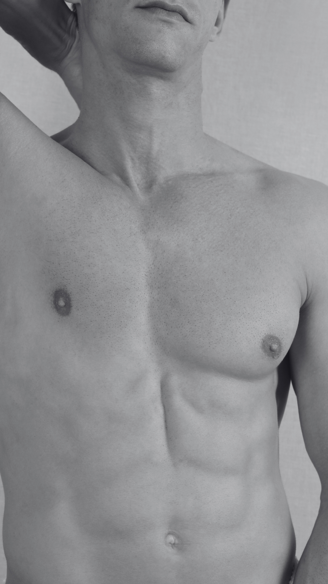 Close-up black and white photo of a shirtless man showing his torso and part of his face, with one arm raised behind his head.