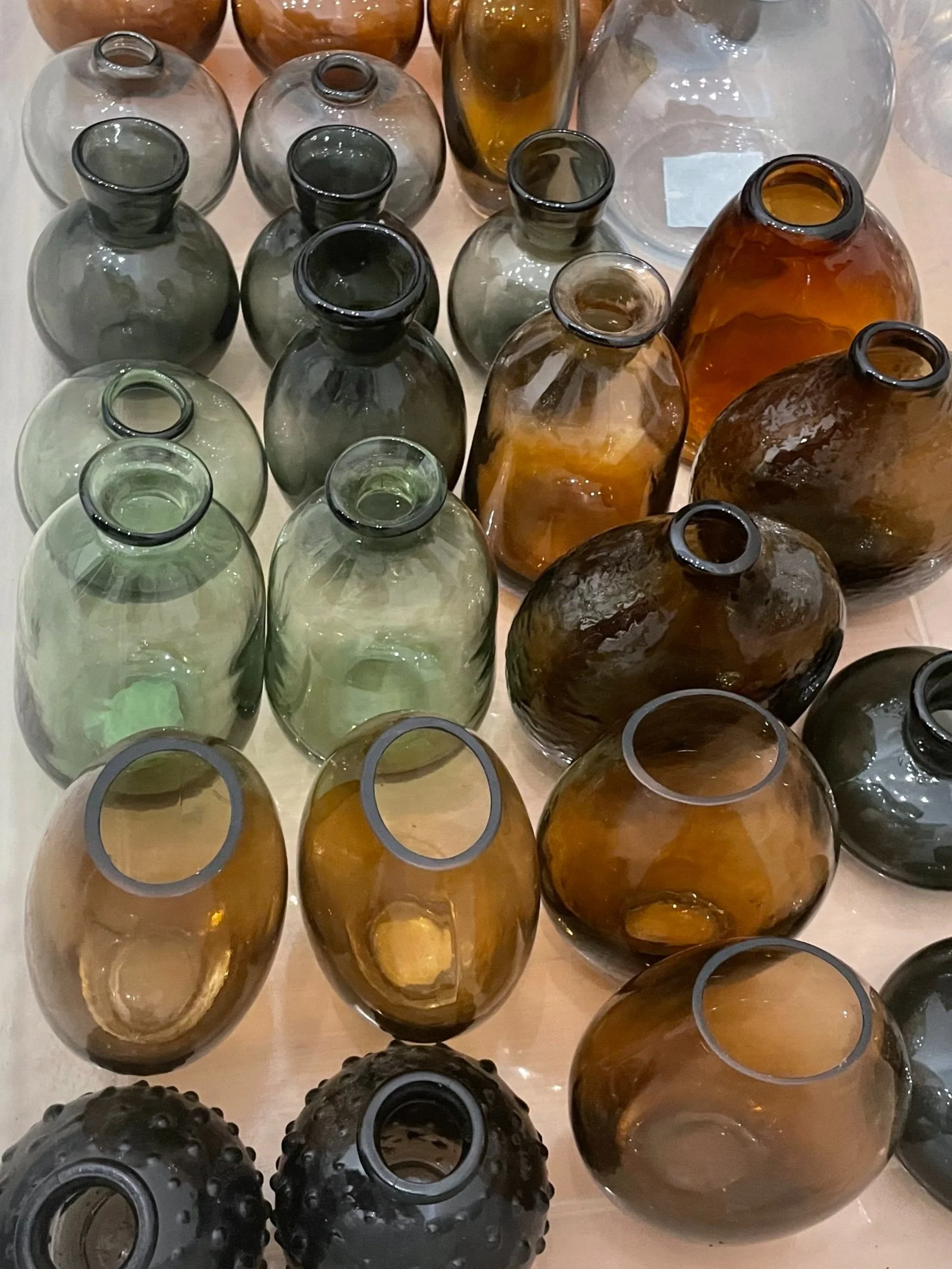 Collection of various glass vases in different shapes, sizes, and colors, including clear, green, amber, and dark hues.