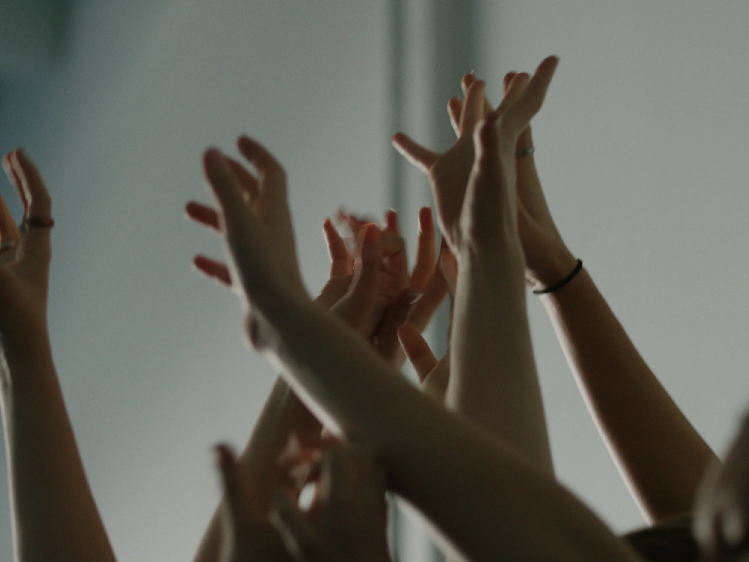 Multiple hands raised in the air, gesturing with various finger positions against a plain background.