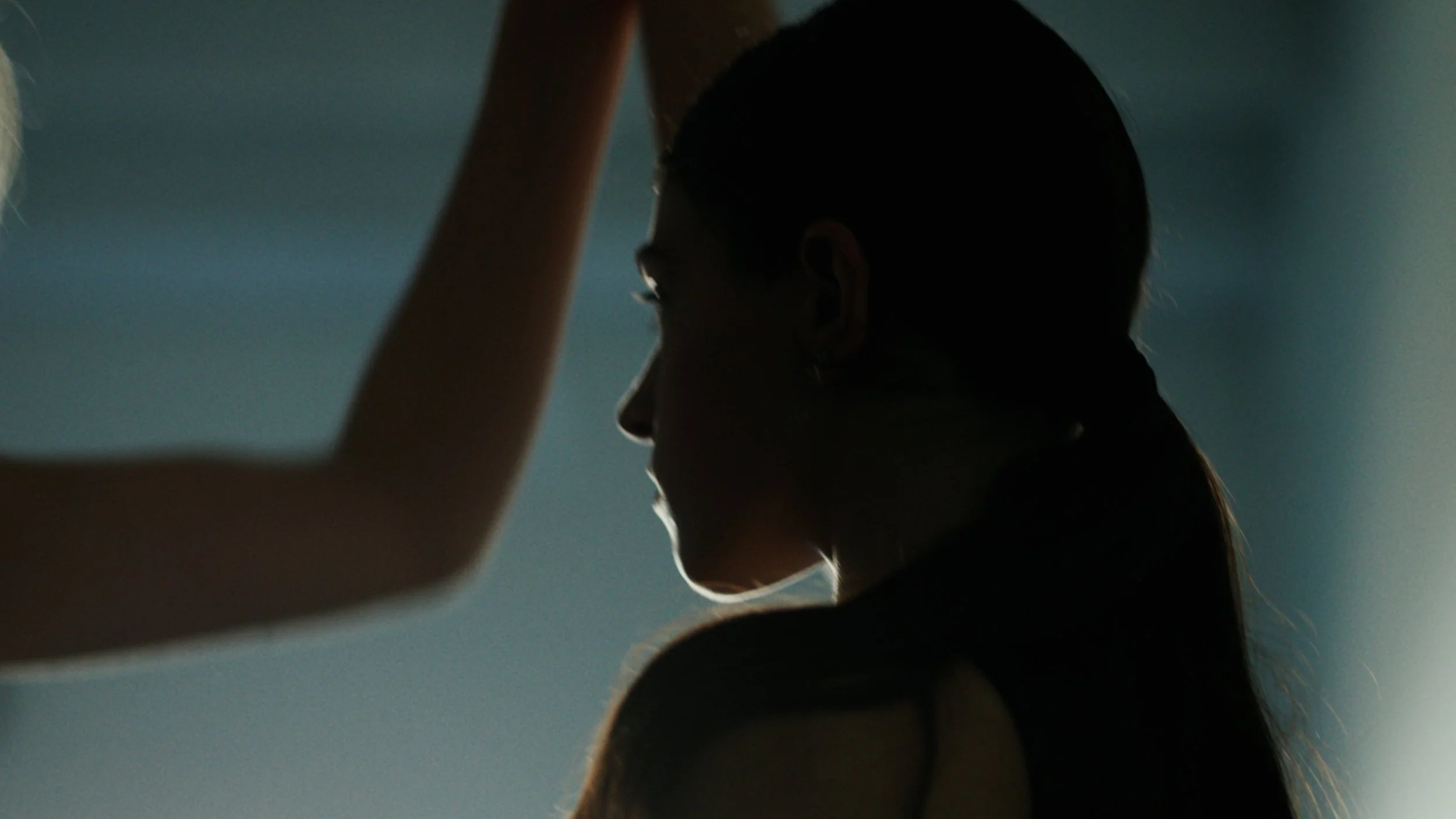 Silhouette of a woman with long hair in pigtails, seen in profile, with arms raised