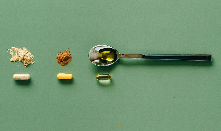 Supplements and a spoon with a liquid supplement on a green background