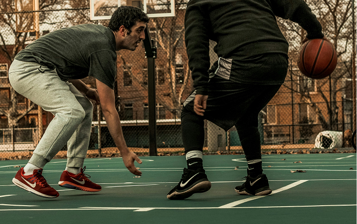 Two men playing basketball on an outdoor court, one dribbling the ball while the other defends.
