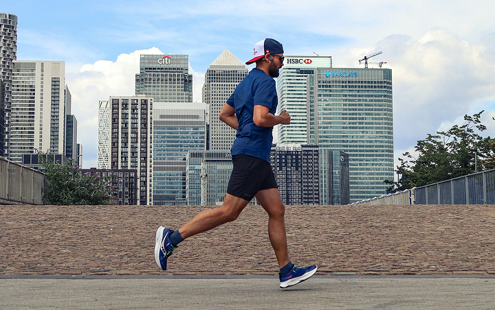 A man running outdoors on a paved path with a city skyline in the background.