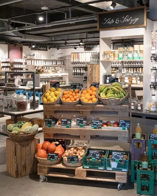 Gemüse- und Obststände in einem Geschäft, darunter Zitronen, Orangen, Bananen, Äpfel, Zwiebeln und andere frische Produkte.