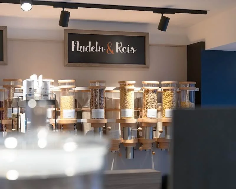 Spenderregale mit verschiedenen Pasta- und Reissorten in einem Lebensmittelladen, mit einem Schilder mit der Aufschrift "Nudeln & Reis"