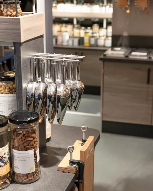 Verschiedene Gläser und Metallbesten in einem Laden, vermutlich für Verkostungen oder Verkaufe von Nüssen.