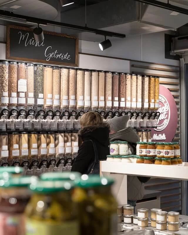 Menschen vor einem Regal mit verschiedenen Getreidesorten und Mahlzeiten in einem Geschäft oder Supermarkt.