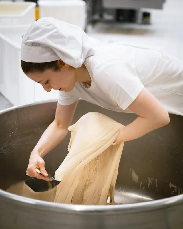 Backfrau beim Teigknette in einer großen runden Metallschüssel in einer Bäckerei