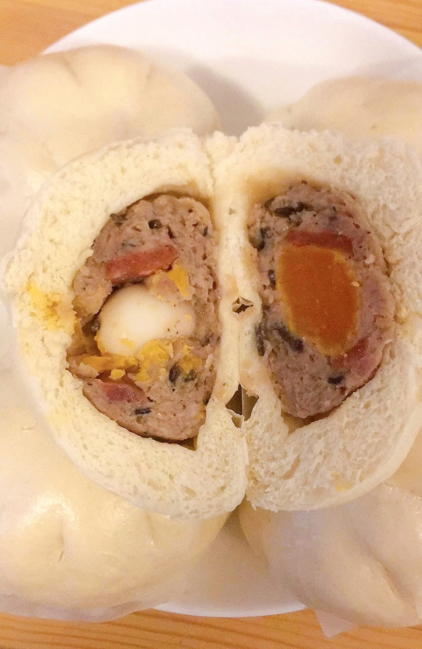 Cross-section of a steamed bun filled with seasoned ground meat, a quail egg, and a salted egg yolk.