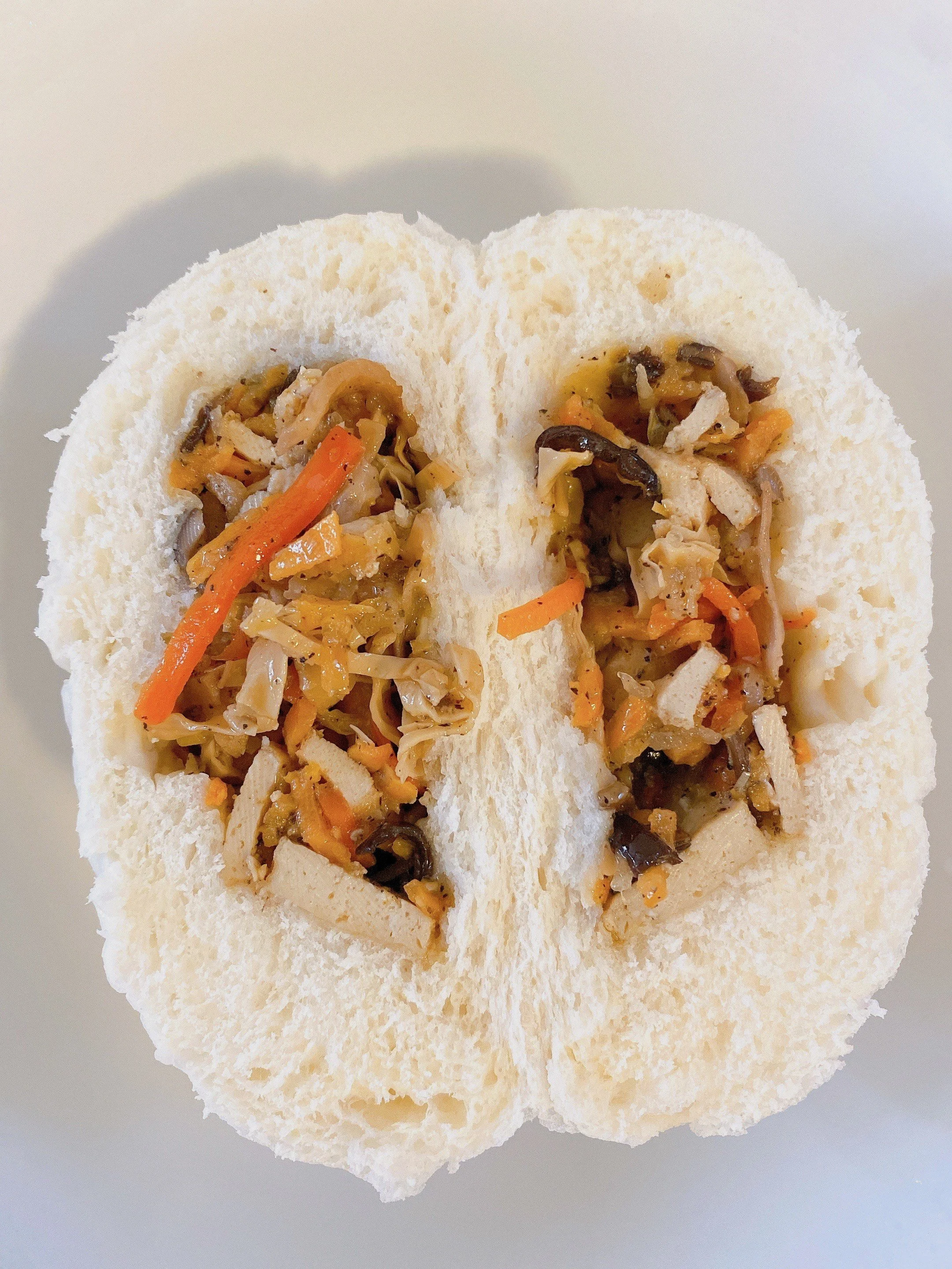 Steamed white bun filled with mixed vegetables, including carrots, mushrooms, and cabbage on a white plate.