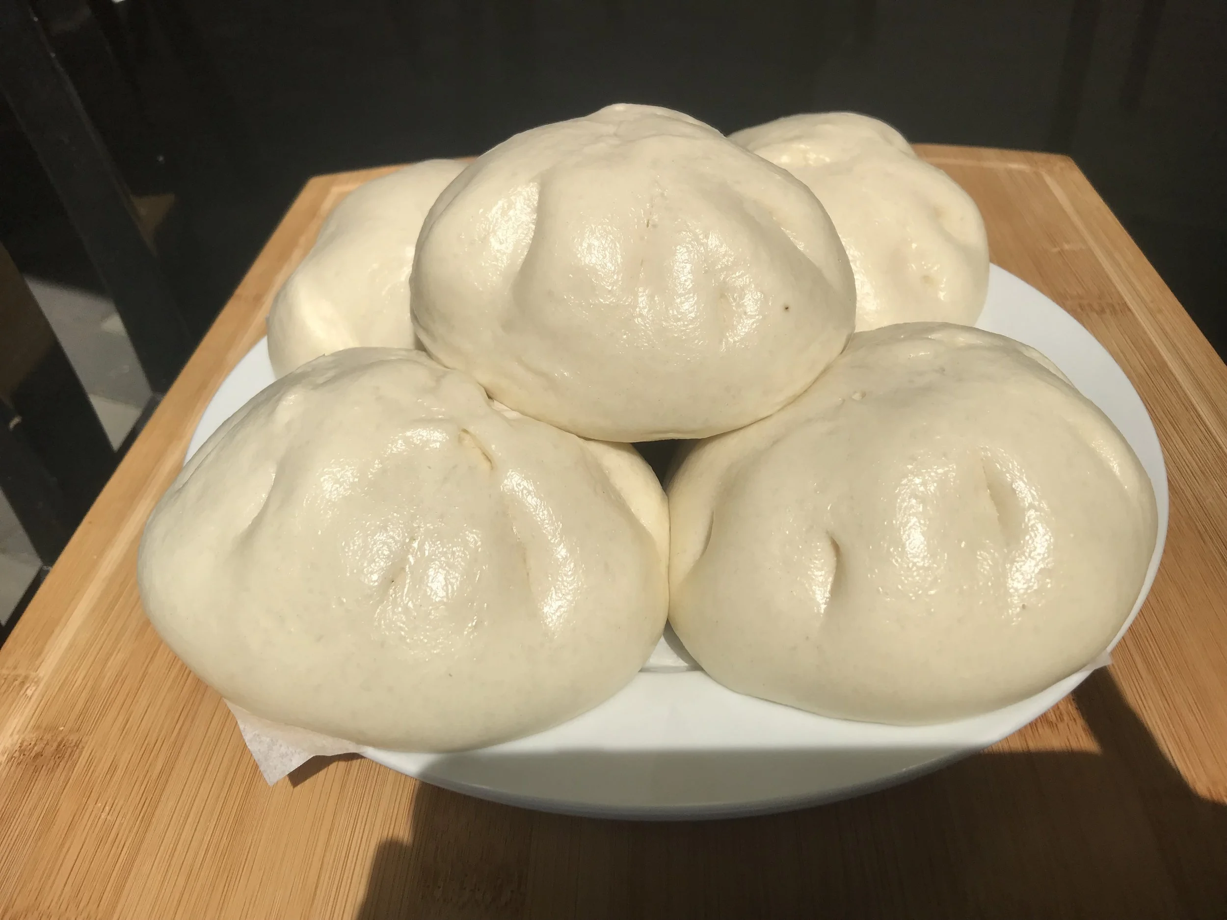 Six uncooked steamed buns on a white plate