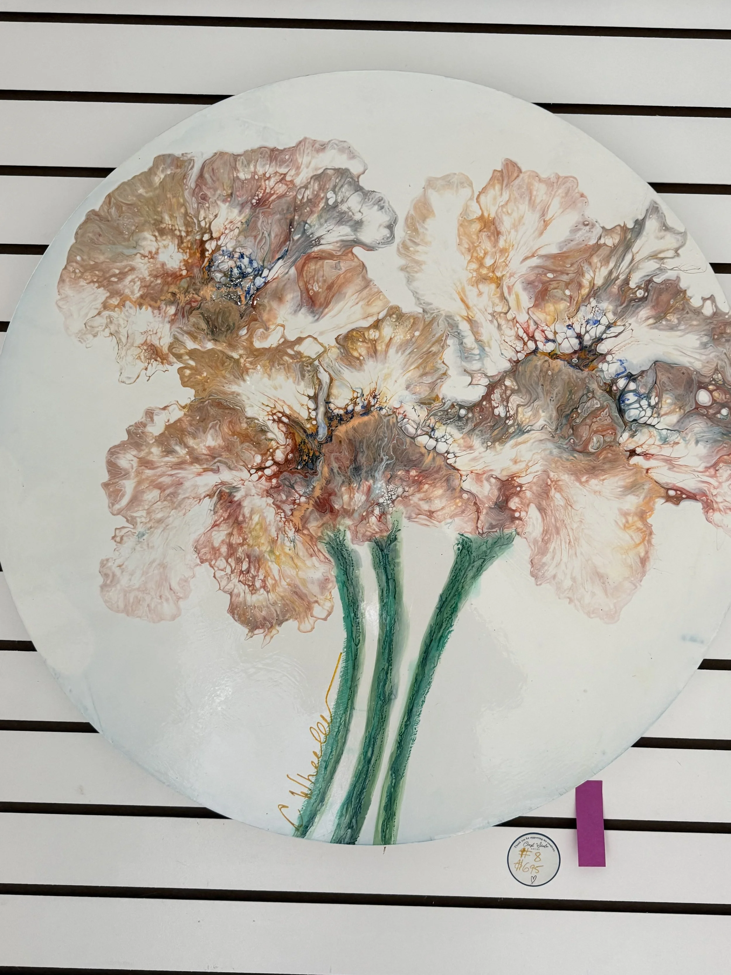 A round white canvas featuring an abstract floral painting with orange, gray, and brown colors, along with green stems, displayed on a slatted wall.