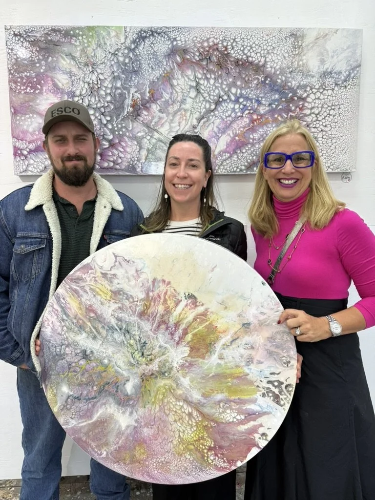 Cheryl Wheeler with two collectors holding a round pink and gold abstract painting