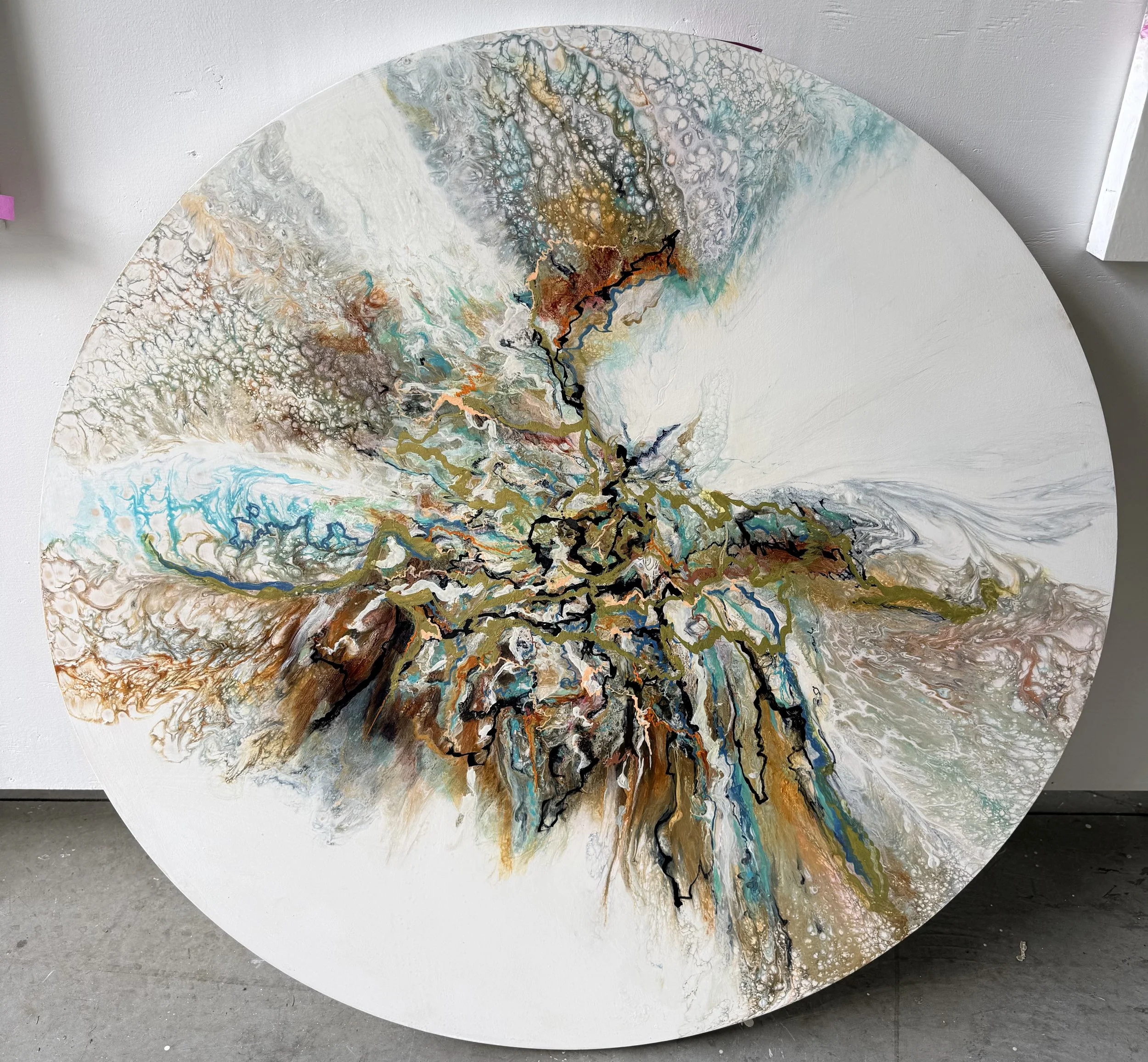 Abstract circular art piece with multicolored flowing patterns, near white wall and gray concrete floor.