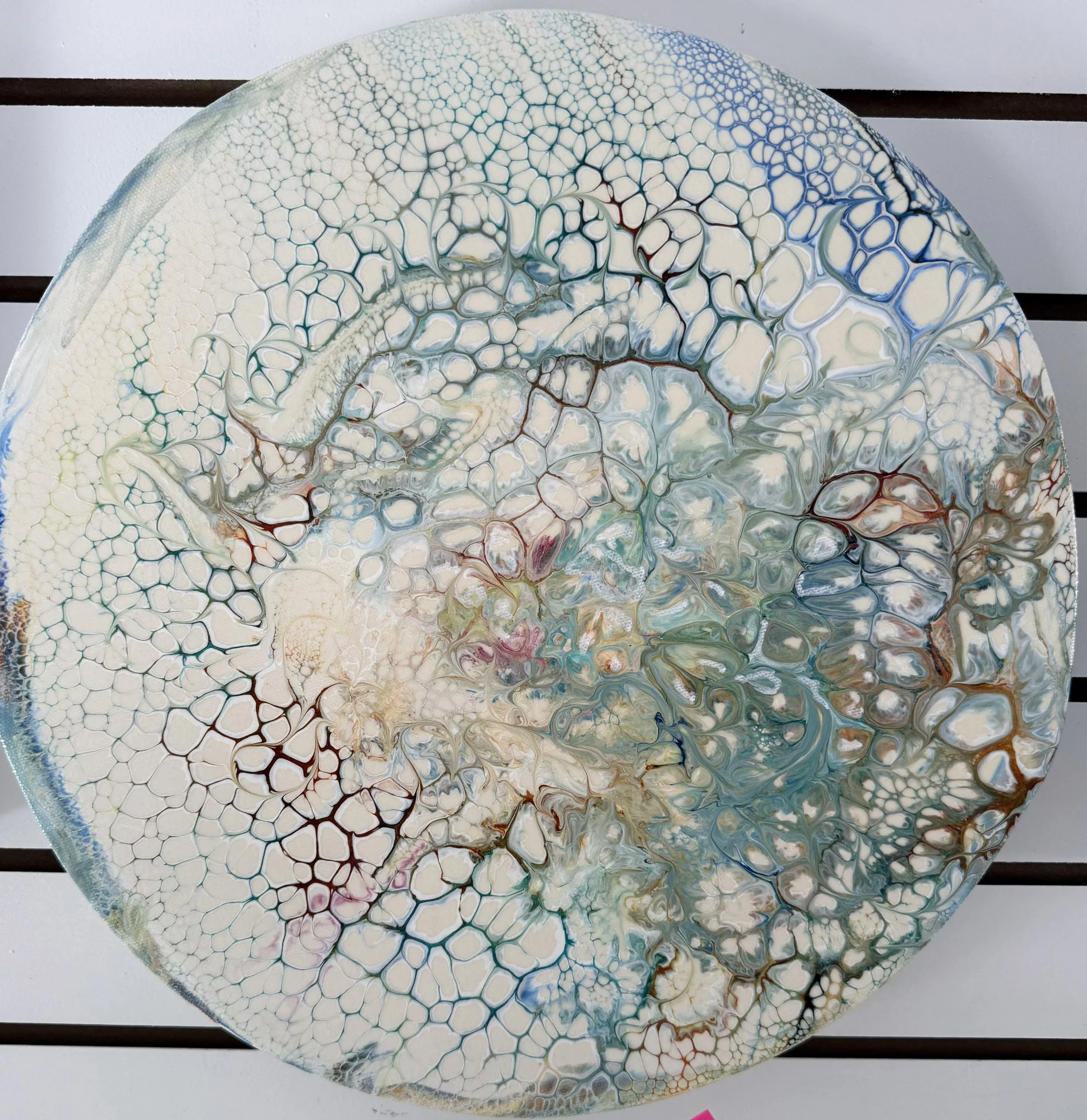 Round abstract artwork with interconnected bubble-like patterns in shades of white, blue, green, and red, resting on a slatted stand.