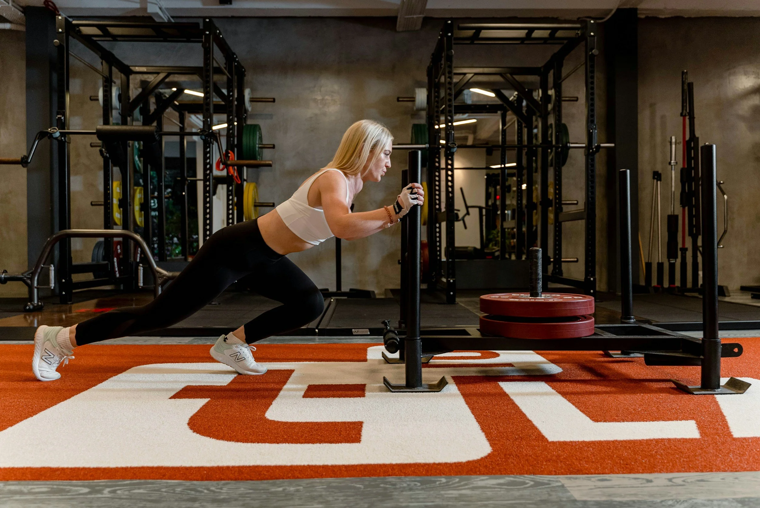 Empwoered By Science: A woman doing a push exercise on a sled push machine in a gym.