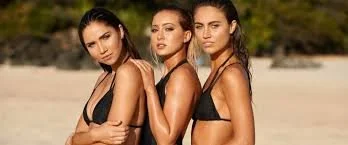 Three women in black swimsuits posing outdoors on a sunny day.