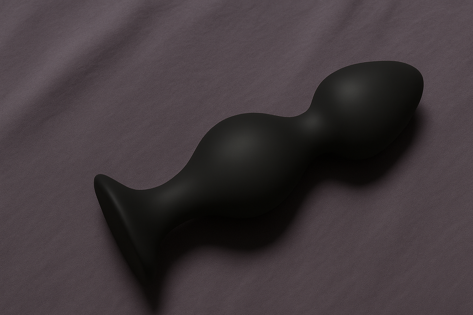 A black, curved, ergonomic vibrator resting on a purple fabric surface.