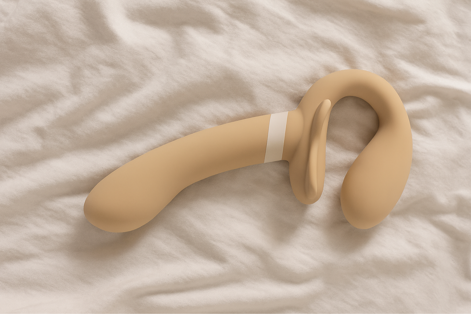 A beige-colored silicone prostate massager with a curved shape and a loop handle, lying on a white fabric surface.