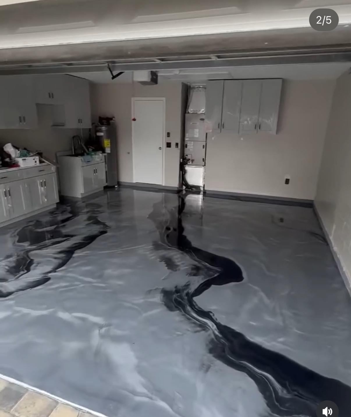 Garage with black and gray marbled epoxy flooring, white cabinets on one wall, and various appliances including a water heater and HVAC unit.