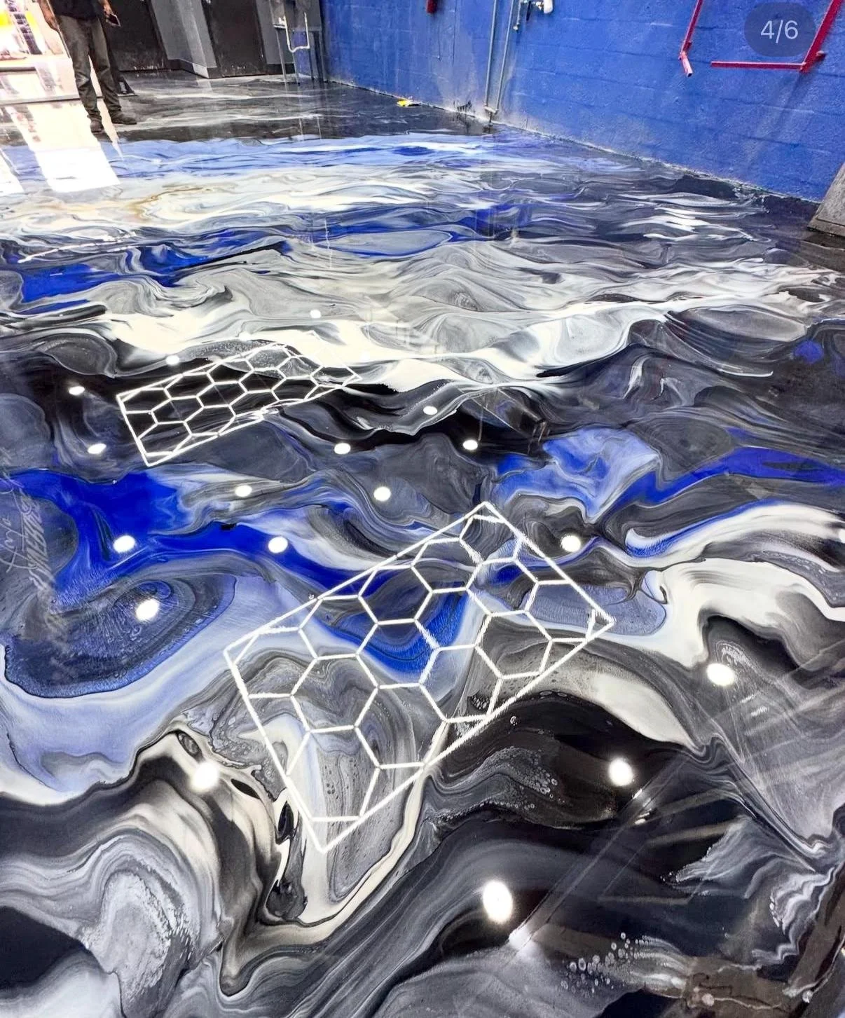 Abstract marble floor with black, white, and blue swirls, illuminated by small round LED lights; two white geometric honeycomb sculptures resting on the surface.
