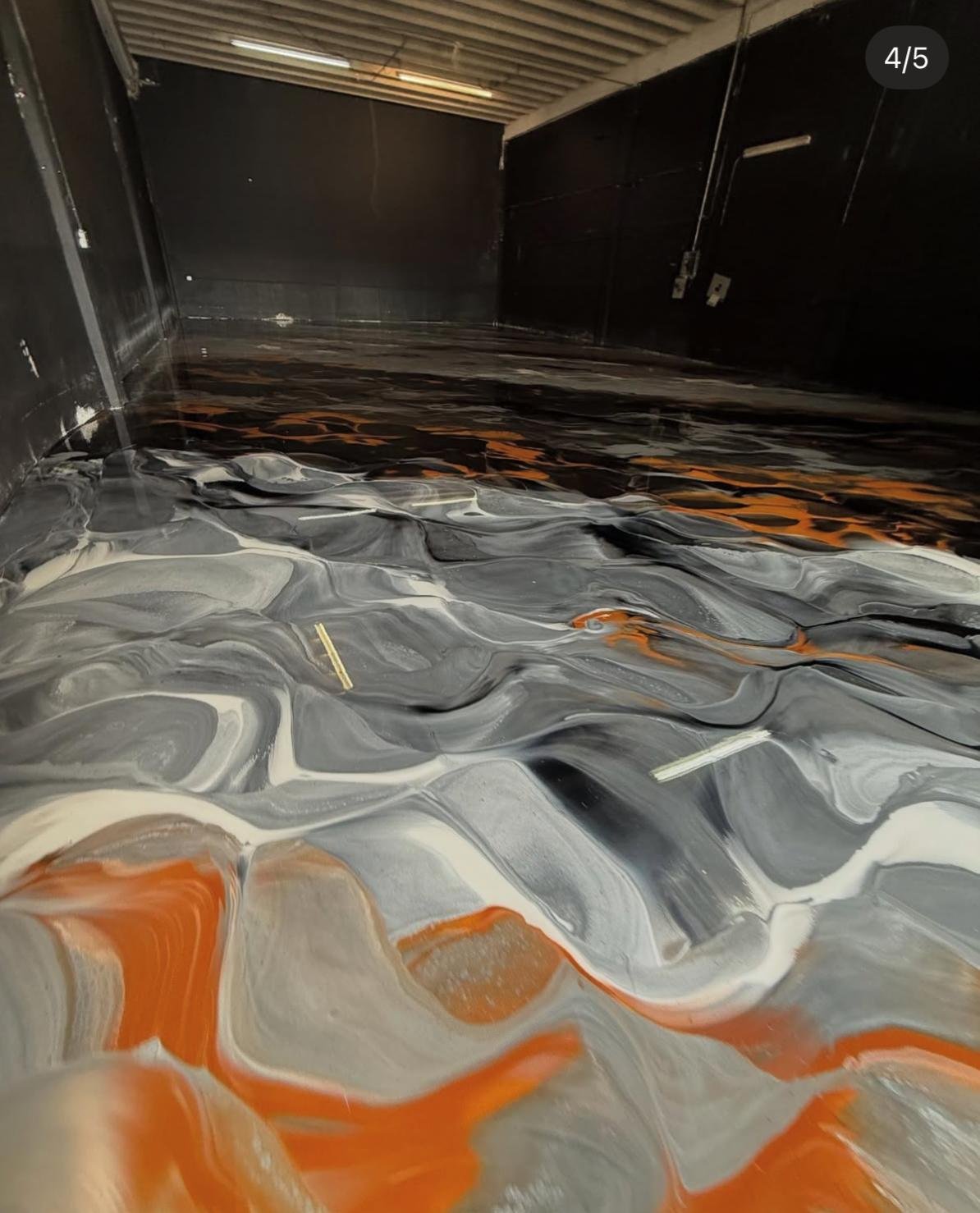Interior of a room with a black wall and a floor with a swirling, marbled pattern in shades of black, white, gray, and orange.