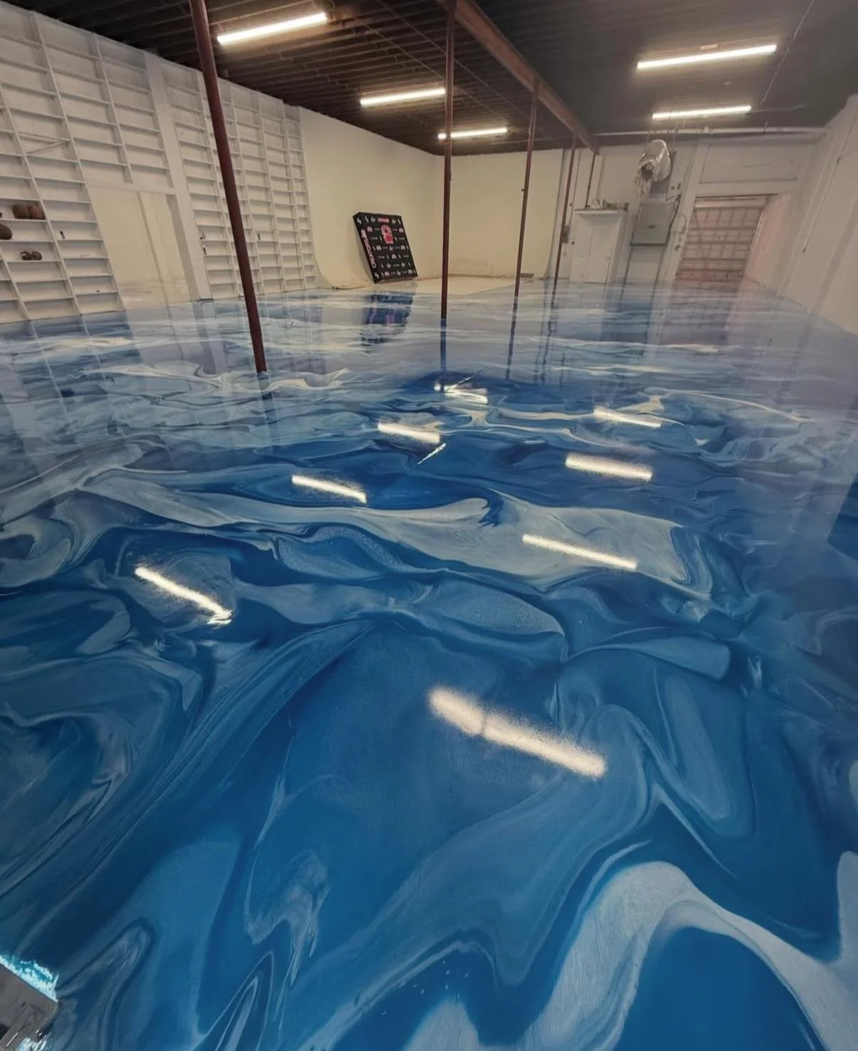 An indoor space with artificial blue water covering the floor, creating a resin or epoxy flooring effect.