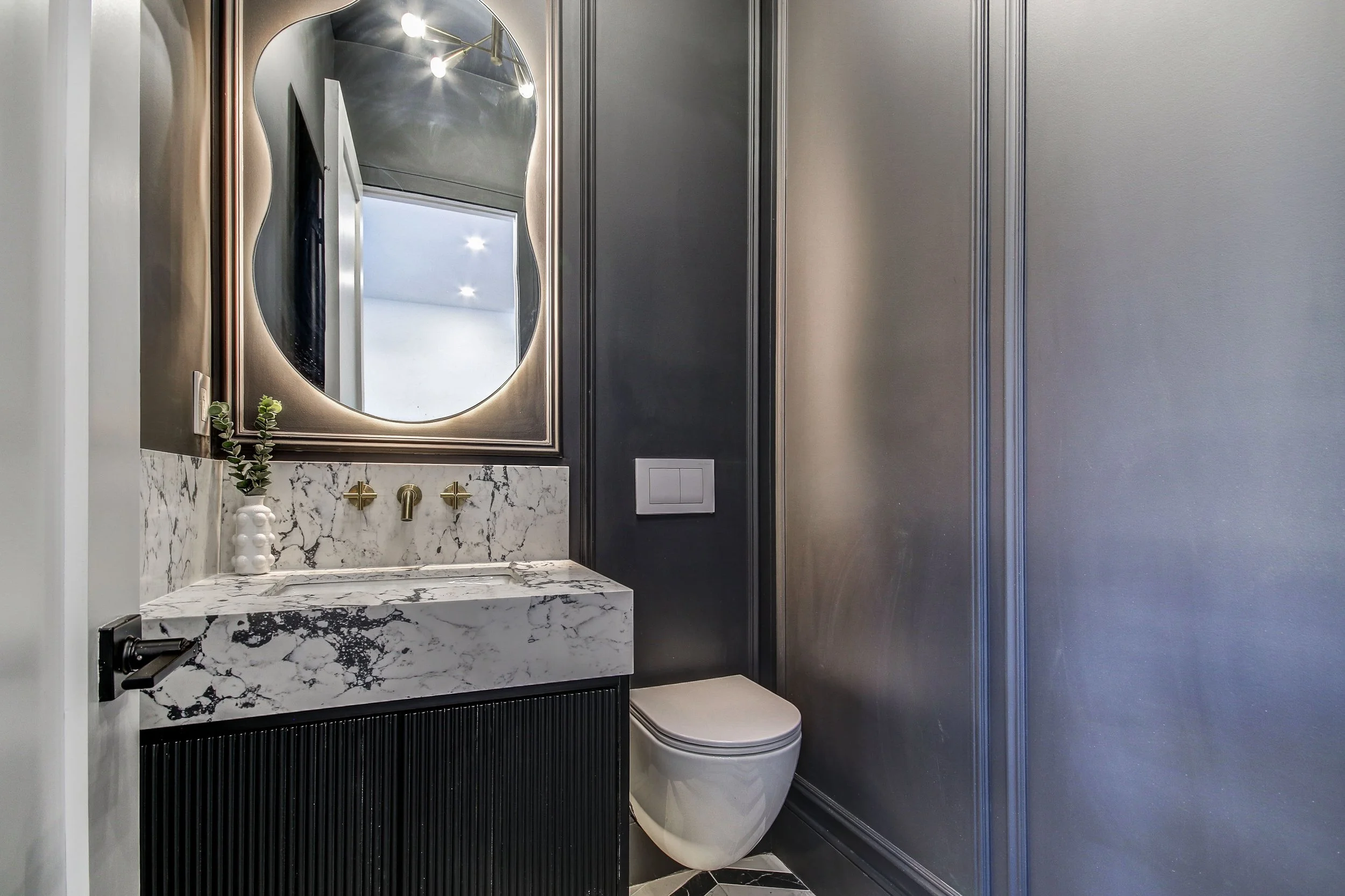 Modern bathroom with marble vanity, circular mirror, gold fixtures, and sleek gray walls.