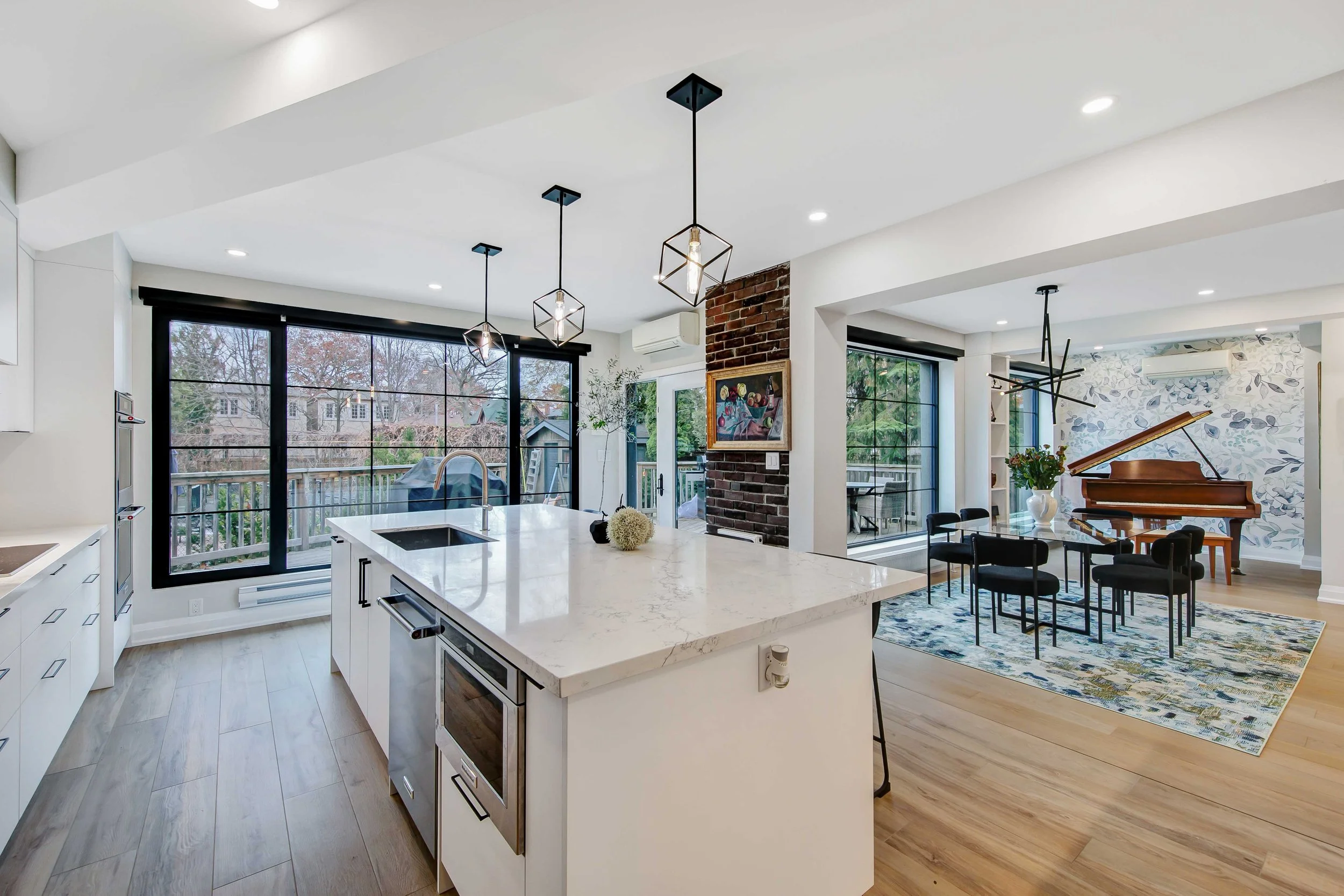 Open-concept kitchen and living room with large windows, modern lighting, and a piano in the background.