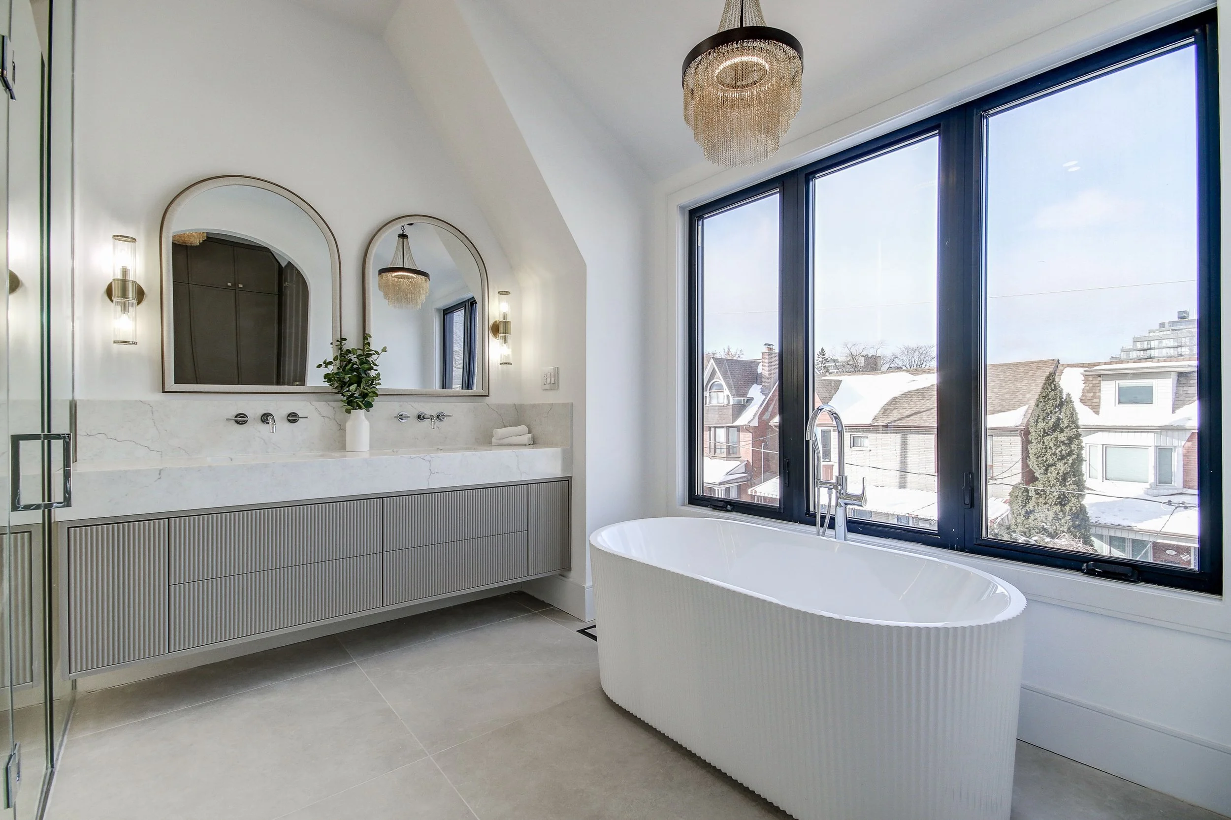 Modern bathroom with large windows, a freestanding bathtub, a marble vanity with double sinks, and minimal decor.
