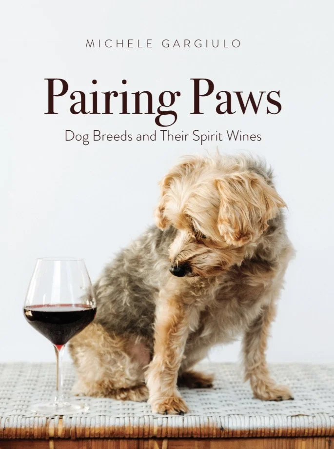 Book cover titled 'Pairing Paws: Dog Breeds and Their Spirit Wines' by Michele Gargiulo, featuring a small, fluffy, tan and gray dog sitting next to a glass of red wine on a textured surface.