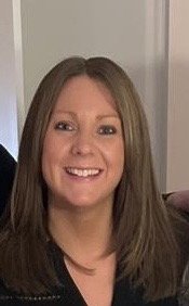 A woman with shoulder-length brown hair smiling in a home setting.