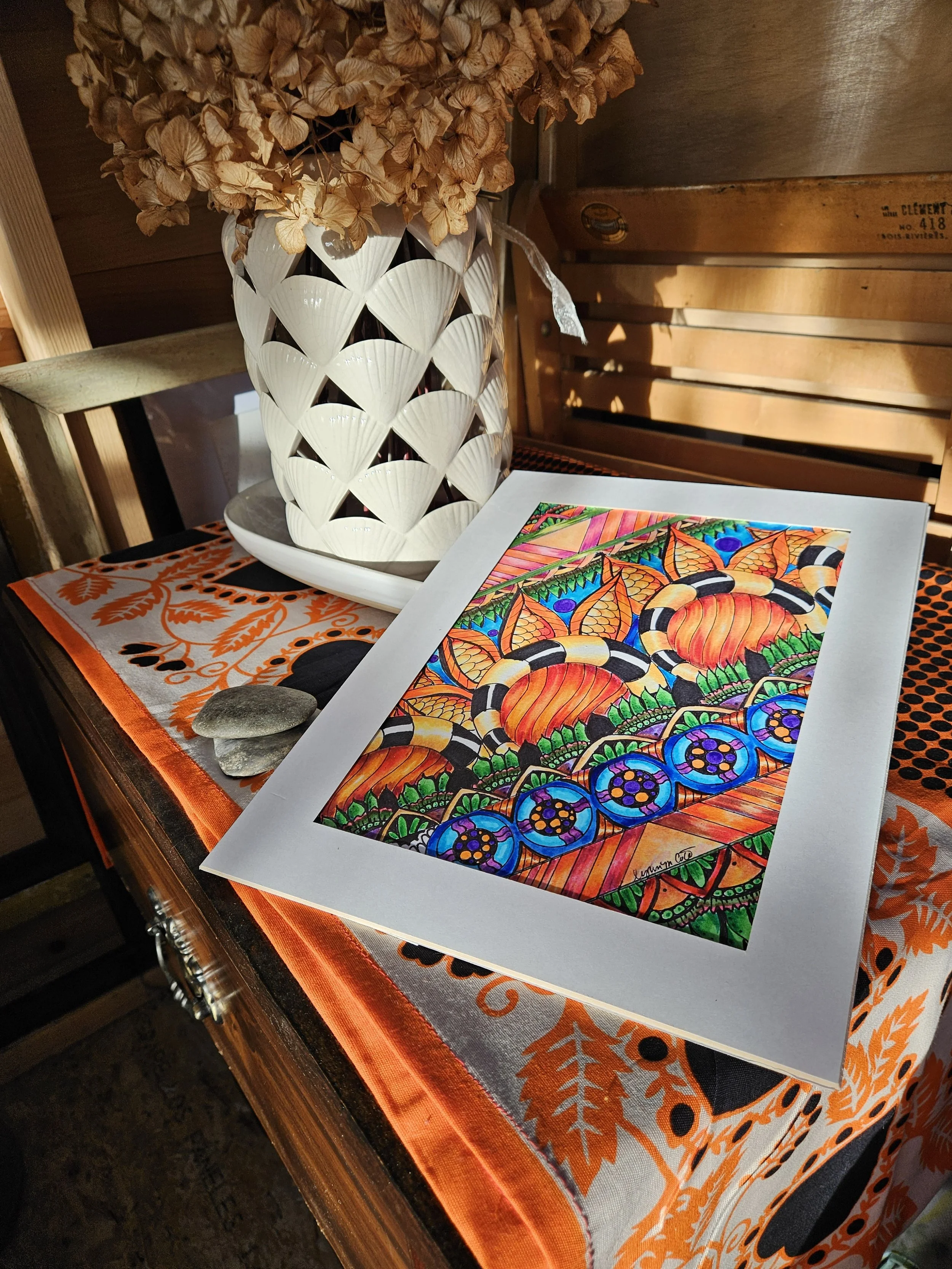Colorful, abstract artwork with orange, green, blue, and black patterns, placed on a table with an orange and white patterned tablecloth.