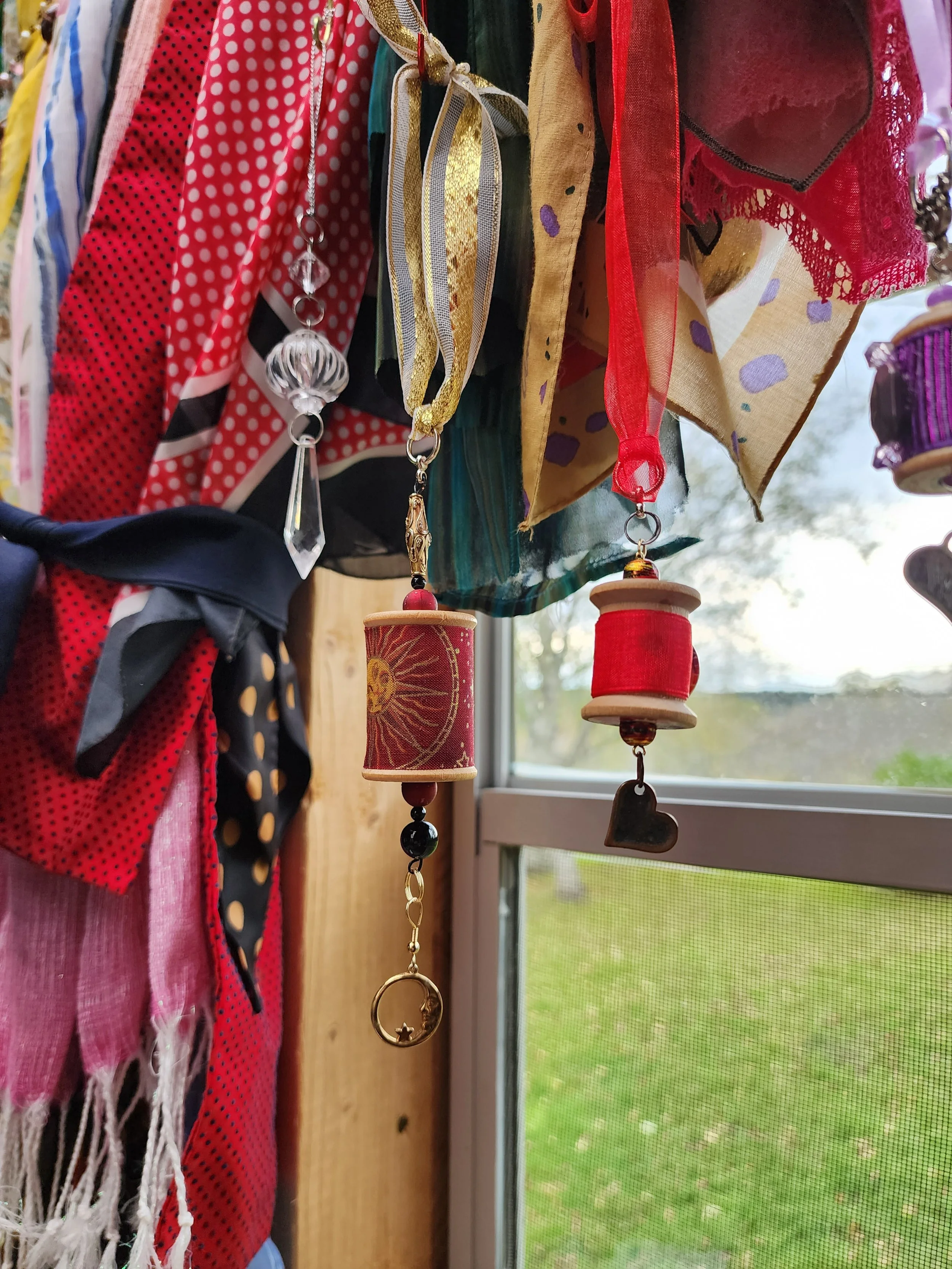 Colorful scarves and jewelry hanging near a window, with a view of trees outside.