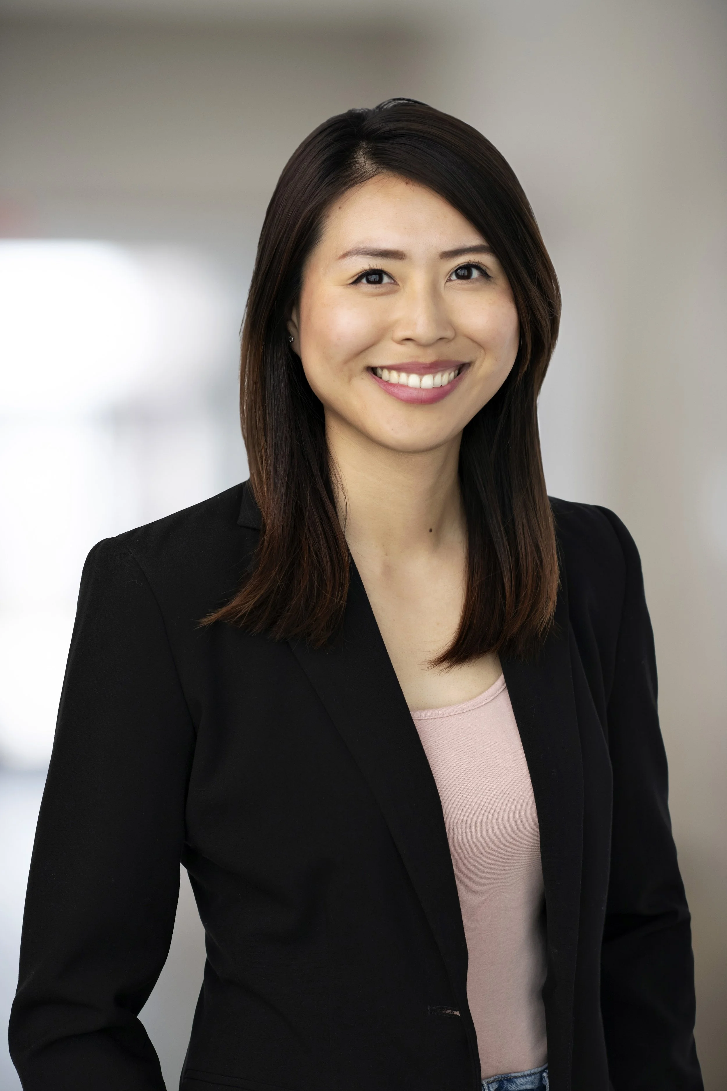 Portrait of a smiling woman with shoulder-length dark hair wearing a black blazer and pink top.