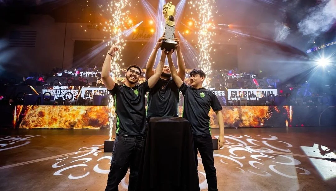 Three esports players celebrating with a trophy on stage, with fireworks and bright lights in the background, after winning a tournament.