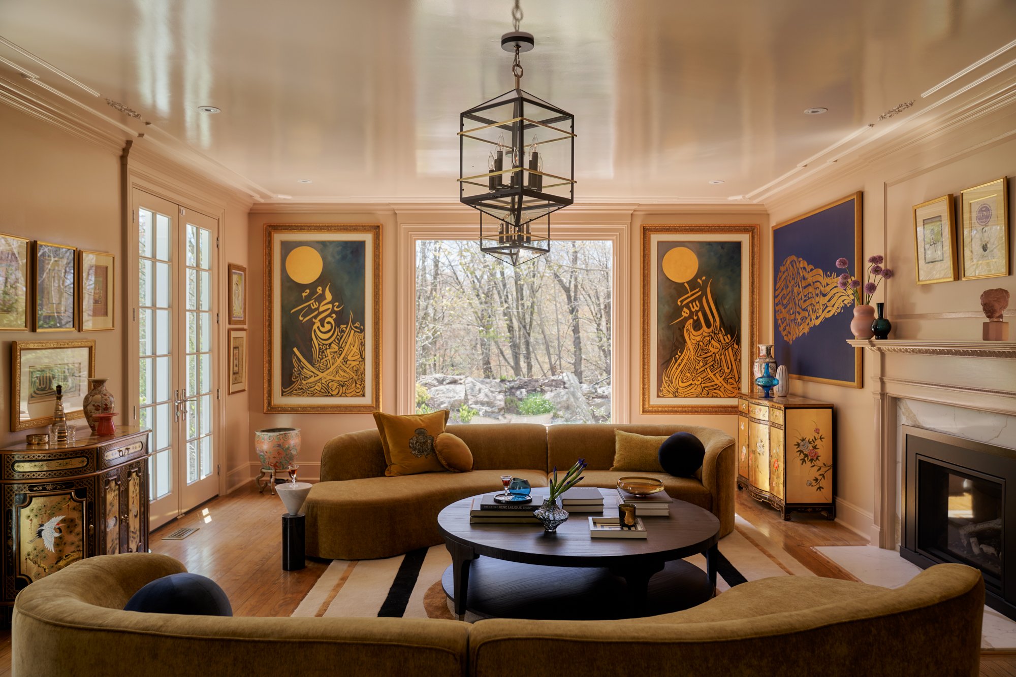 This jewel-toned sitting room celebrates global elegance through a confluence of calligraphy, chinoiserie, and midcentury-inspired form. A custom velvet curved sofa grounds the space in saturated mustard, while large-scale Islamic calligraphy adds sp