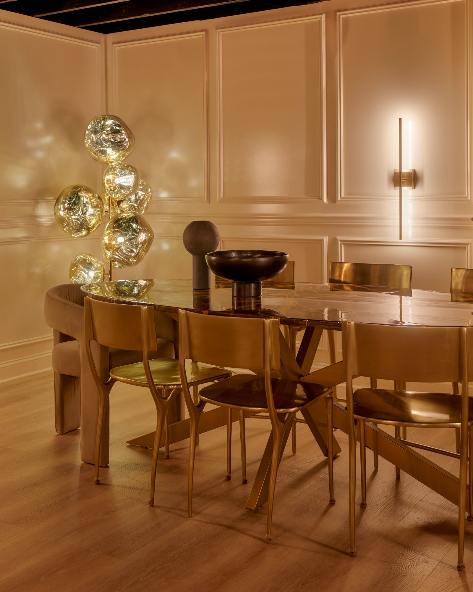 This moody, luminous dining space reimagines the basement as a destination for design. Wrapped in high-gloss paneling and anchored by a sculptural brass dining table, the room plays with reflection and form. Smoky blown-glass lighting and molten-gold