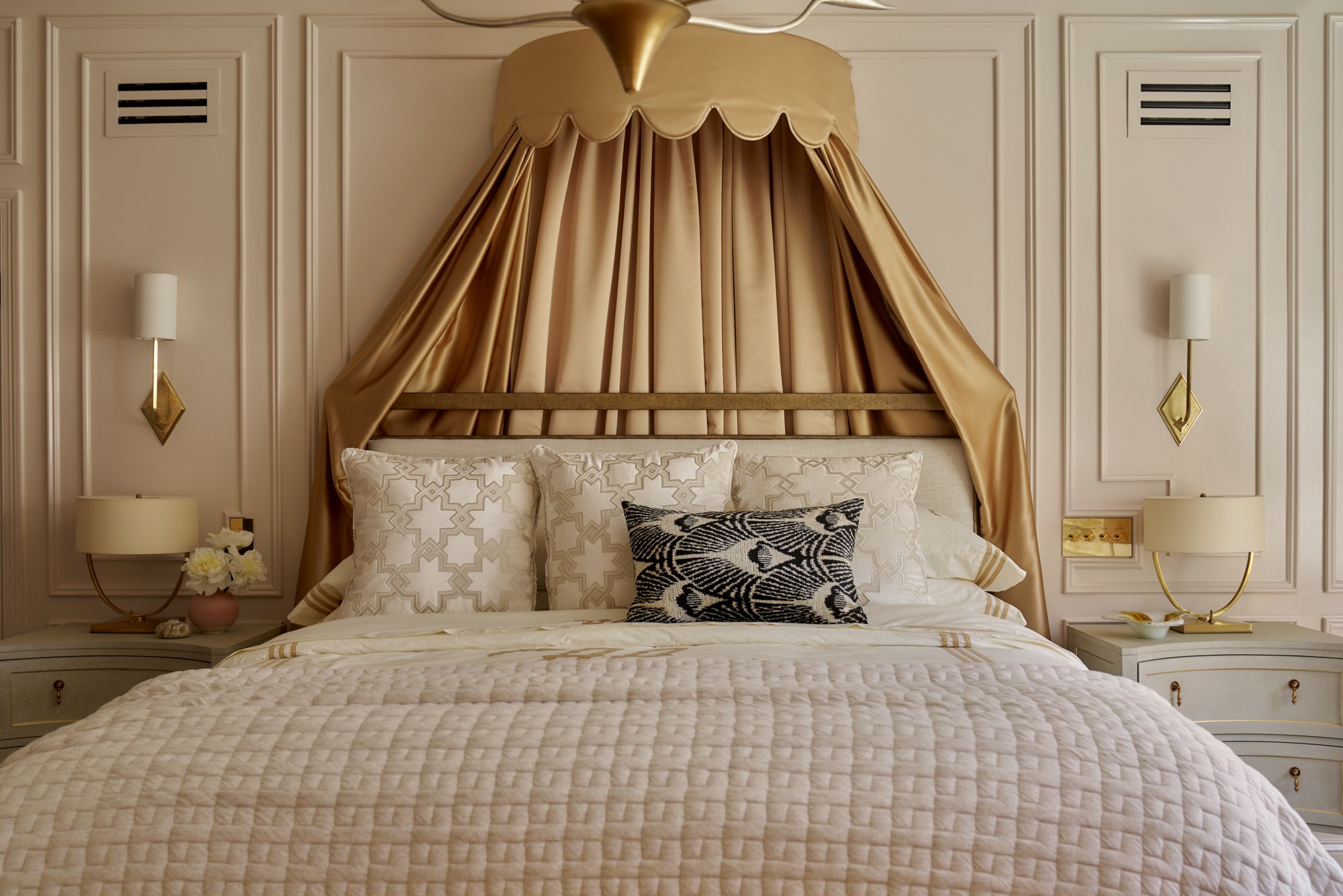 This bespoke bedroom centers around a tailored canopy in lustrous camel-toned silk, scalloped and draped for a sense of drama and softness. Layered textiles in embroidered linen and cut velvet add depth and touchable luxury, anchored by a singular pe