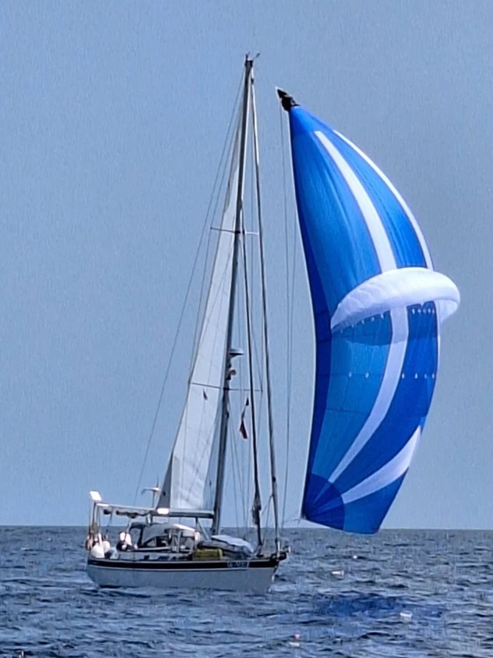 A sailboat on open water with a large blue and white inflatable spinnaker sail.