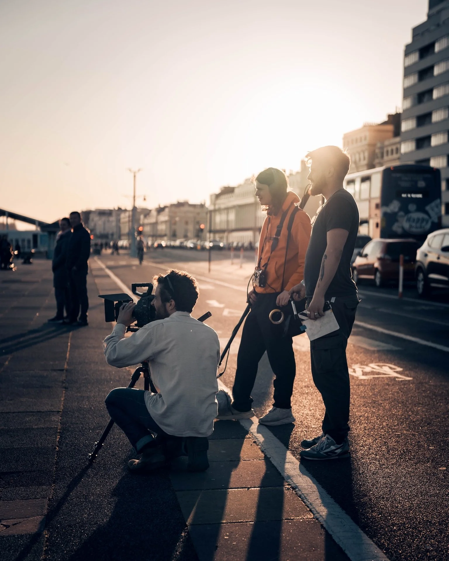Filmmakers and crew filming scenes on a city street at sunset.